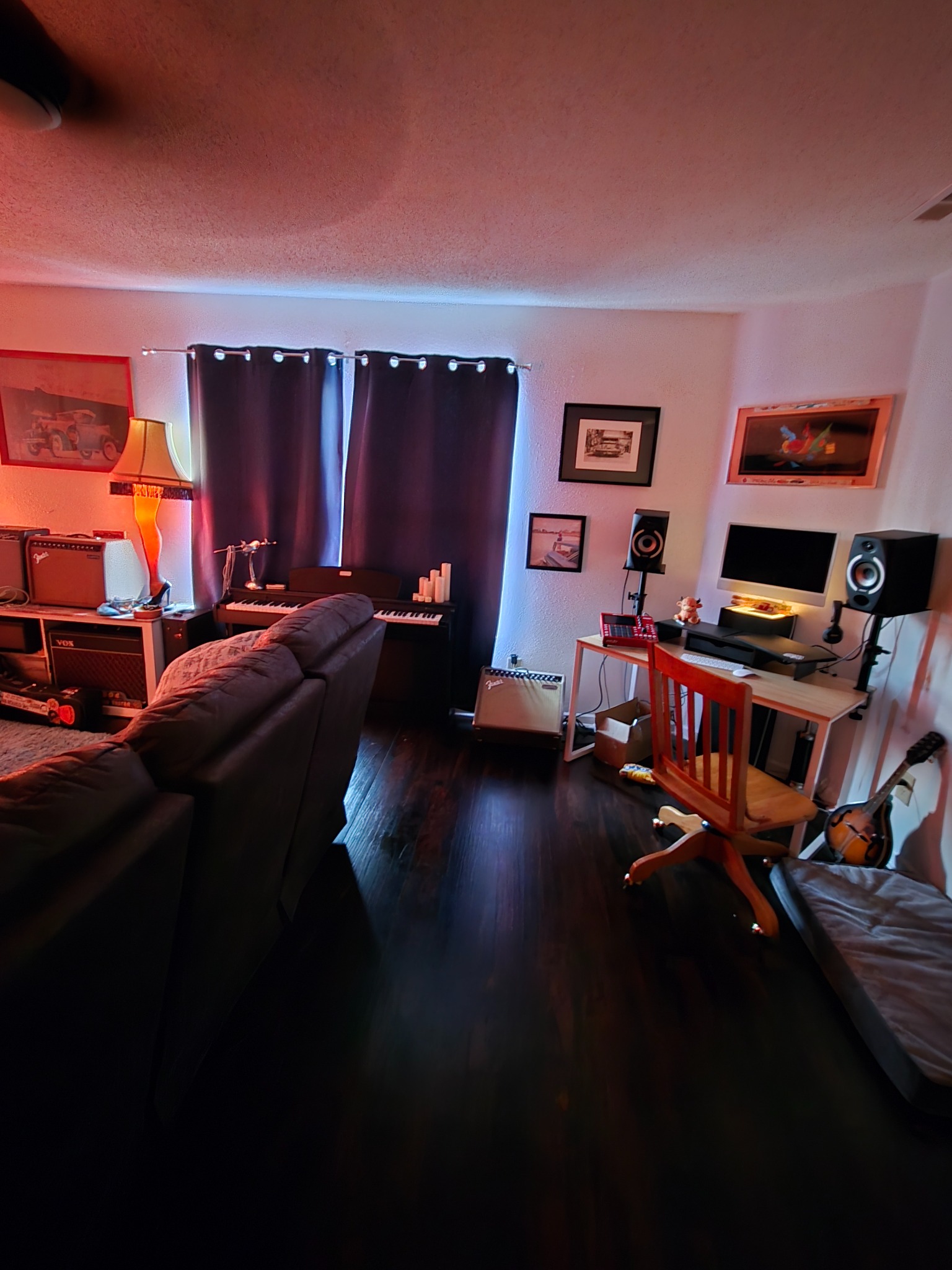 A small creative studio setup with guitar amps, keyboard, speakers, computer desk, and recording gear.